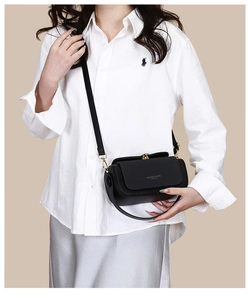 Detail of black leather crossbody bag with woven texture lid and golden metal buckle