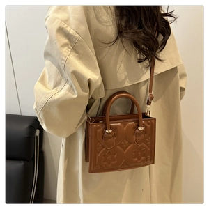 Brown embossed leather handbag with floral pattern carried by a model in a beige coat