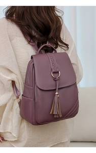 Side view of mauve PU leather backpack featuring woven flap and tassel accent on model