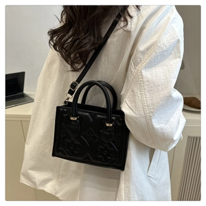 Detail of black crossbody bag featuring floral embossed texture and gold metal accents