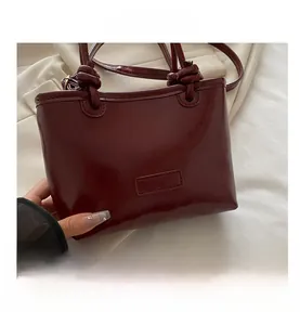Detail view of burgundy tote bag showing knotted handles and glossy faux leather texture