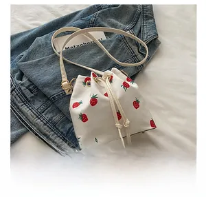 Detail of white strawberry canvas bucket bag with gold hardware and phone for size comparison