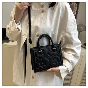 Detail of black embossed floral pattern on a compact crossbody bag with gold hardware