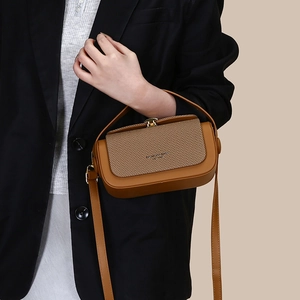 Detail of brown leather handbag featuring a textured woven flap and gold metal hardware