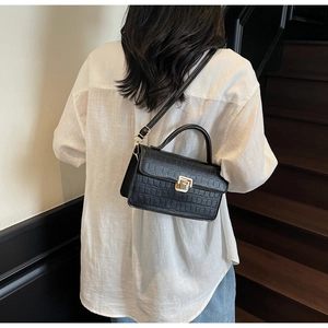 Detail of black faux crocodile texture on handbag with gold metal clasp in lifestyle setting
