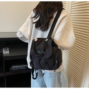 Detail of black nylon backpack featuring contrast wrap handles and letter embroidery