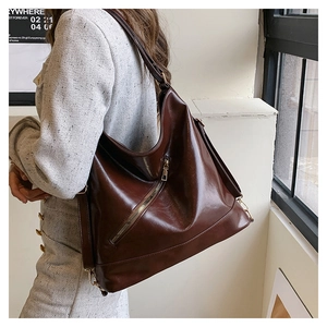 Detail of glossy brown leather tote bag showing front zipper pocket and wide strap