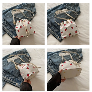 Multi-angle view of a white drawstring bucket bag with strawberry prints and metal feet
