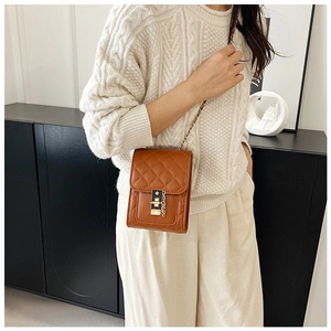 Detail of brown quilted crossbody bag with metal twist lock and chain strap on a model