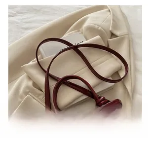 Detail view of burgundy glossy leather tote bag with knotted strap on cream blazer