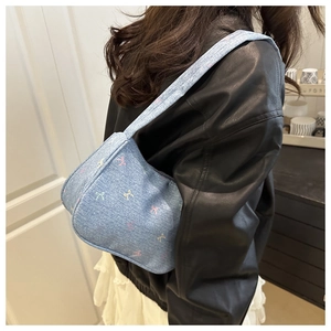 Light blue denim underarm bag with butterfly pattern shown on a model's shoulder