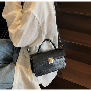 Detail of black faux leather mini bag with crocodile texture and gold clasp