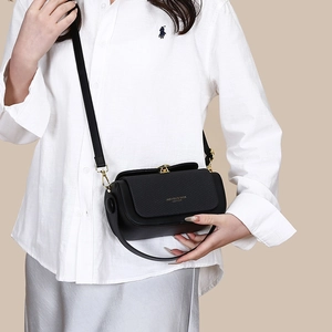 Close-up of black leather crossbody bag with woven texture lid and golden lettering