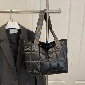 Black quilted puffer tote bag with blue patterned handles on a display rack