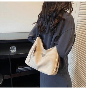 Detail of soft beige suede tote with triangular metal logo and brown knotted leather zip pull