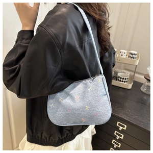 Model wearing a light blue denim underarm bag with colorful ribbon bow embroidery