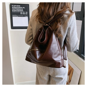 Detail view of deep chocolate faux leather backpack with metallic zippers on grey blazer