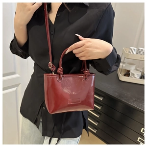 Detail of a dark red patent leather mini square bag with dual handles and crossbody strap