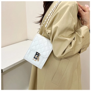 Detail of white quilted crossbody bag with gold-tone buckle and metal chain strap on beige coat