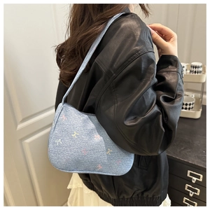Detailed side view of light blue denim underarm bag with colorful embroidered bows