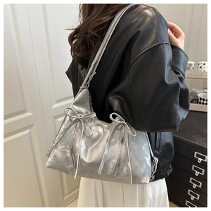 Detailansicht einer silbernen Metall-Schultertasche mit Schleifen und Reißverschlüssen