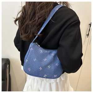 Detail of blue denim underarm bag featuring pink and yellow bow patterns and silver zipper