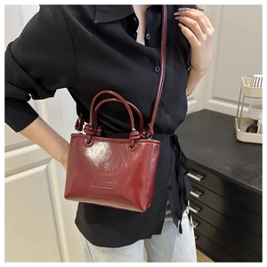 Detail view of wine red glossy leather crossbody bag with knot handle and adjustable strap