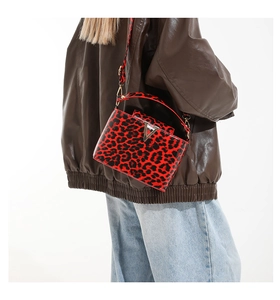 Detail of red leopard print patent leather handbag with V-shaped metal buckle on a model