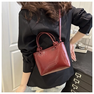 Detail of burgundy glossy patent leather square bag with knotted handles and thin strap