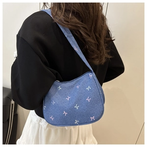 Detail of blue denim shoulder bag featuring pink and white embroidered bows on the surface