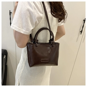 Detail of dark brown glossy leather handbag with unique knotted handle design and strap