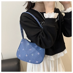Detail of blue denim shoulder bag featuring pink bow embroidery and zipper closure