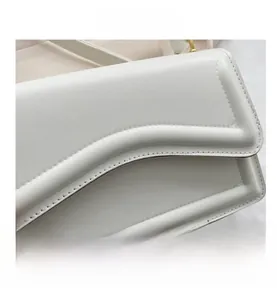 Detail of white leather bag featuring wavy flap design and gold-tone metal D-ring hardware