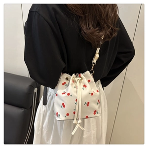 Detail of drawstring bucket bag with red cherry prints and metal eyelet accents