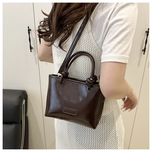 Detail of dark brown glossy square bag featuring creative knot handle and long strap