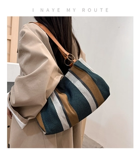 Detail of striped canvas tote bag with brown leather straps and gold metal ring hardware