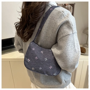 Detail of dark blue denim underarm bag with colorful bow embroidery worn by model