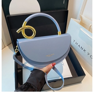 Nahaufnahme der Morandi-blauen Satteltasche aus Leder mit goldenem Griff in einer Geschenkbox