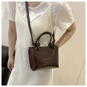 Detail of a dark brown mini crossbody bag with knotted handles and polished finish