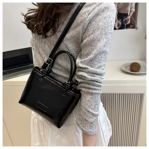 Detail shot of a black glossy crossbody bag with golden hardware on a model