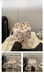 Detail of drawstring bucket bag with red cherry prints and golden metal hardware