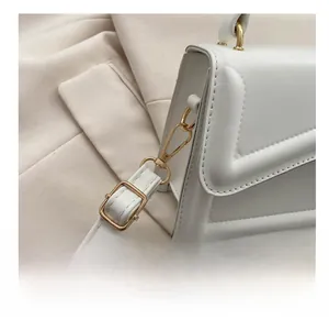 Detail of gold metal hook and V-shaped stitching on white leather crossbody bag
