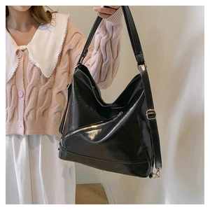 Detail view of large black tote bag featuring glossy texture and gold metal hardware adjustment