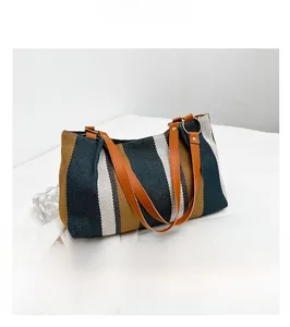 Detail of striped canvas tote bag showing brown leather strap and gold metal ring connection