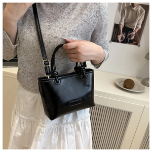 Close-up of a black patent leather square bag paired with a white dress and grey sweater