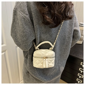 Detail view of a white quilted mini vanity bag with a gold chain and leather handle