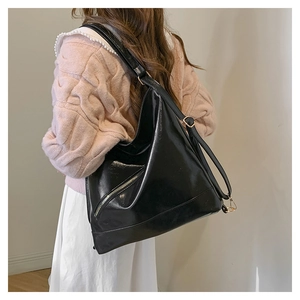 Side view of large black shiny tote bag worn by model, showing capacity and strap detail