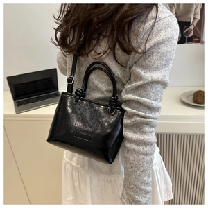 Detail of black glossy crinkled leather shoulder bag with chic cylindrical handle knot