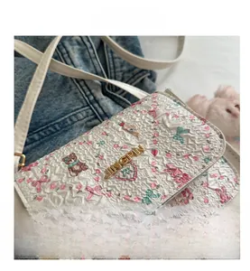Detail of white pleated crossbody bag with floral bear print and metal logo