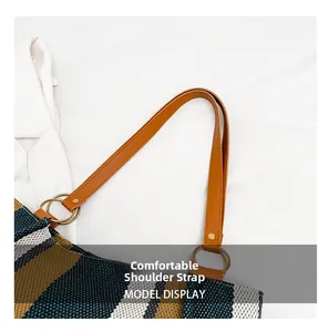 Detail of the brown leather strap and gold metal rings on a striped canvas tote bag